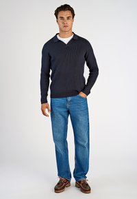 Dunkelblauer gerippter Strickpullover mit Kragen, kombiniert mit hellblauen geraden Jeans und braunen Schnürschuhen. Minimalistisches Design.