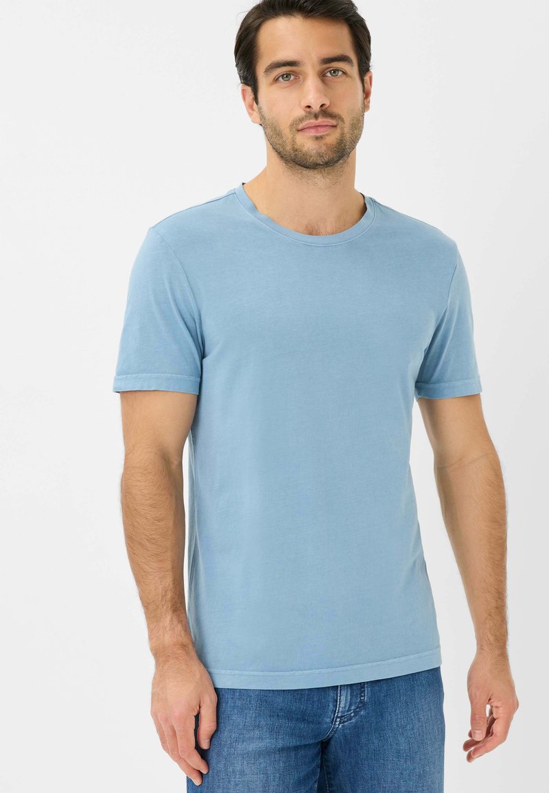 Lyseblå bomulds T-shirt med rund hals og korte ærmer, vist på en person, sammen med blå jeans. Glat tekstur, minimalistisk design.