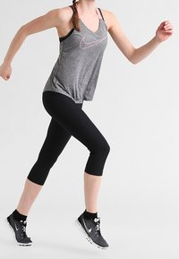 Gray athletic tank top with a pink Nike logo, paired with black capri leggings and black running shoes with white accents.