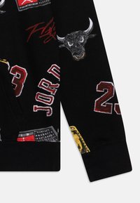 Tissu noir avec broderie rouge du « 23 », du texte « Jordan », une tête de taureau féroce, et une signature rouge « Flight » dans un style sportif.
