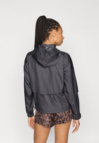 Sort let jakke med hætte, der har en afslappet pasform og elastiske manchetter. Bæres over leopardmønstrede shorts og viser et lagdelt design.