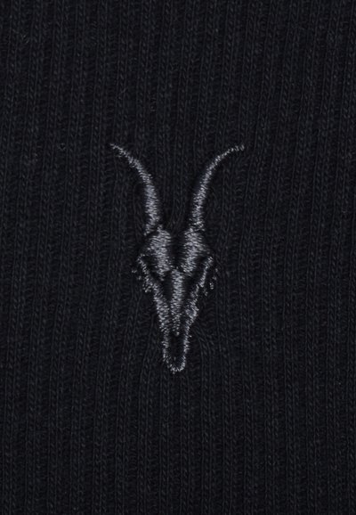 Tissu tricoté noir avec un petit crâne d’animal gris brodé au centre, avec de longues cornes courbées.
