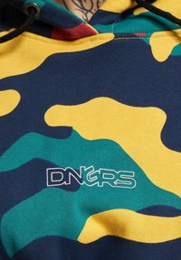 Večbarvna dukserica s kamuflažnim vzorcem v modri, rumeni, zeleni in rdeči; na sprednji strani je bel logotip "DNGRS".