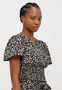 Blusa floreale con sfondo nero decorata con piccoli fiori rosa, blu e beige, maniche corte a palloncino e design a vita cintrata.