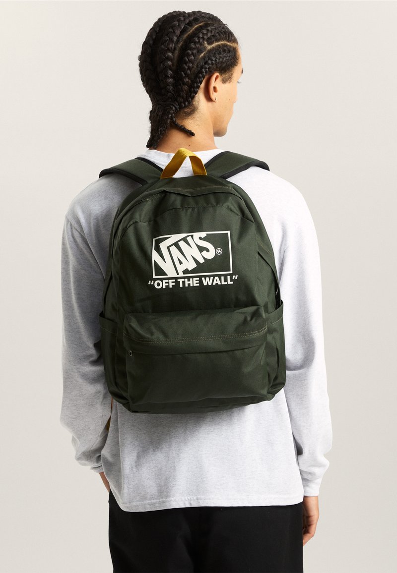 Groene stoffen rugzak met wit Vans-logo, voorzien van verstelbare riemen, een bovenhandvat en een voorvak met rits. Soepele textuur, rechthoekige vorm.