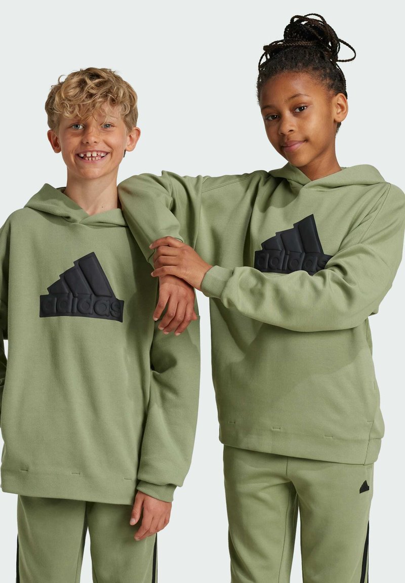Felpe con cappuccio verdi con il logo Adidas testurizzato in nero. Il tessuto sembra morbido e entrambe le persone indossano abiti coordinati, compresi i pantaloni.