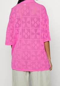 Rosa meshtopp med geometriska diamantmönster och krage. Korta ärmar, avslappnad passform och ett lager av textur.