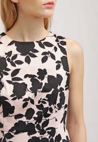 Motif floral noir sur une robe rose clair avec un design sans manches et un col rond, vue de l'épaule vers le haut. Texture lisse.