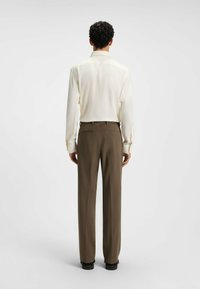 Light cream long-sleeve shirt paired with dark brown tailored trousers. The shirt features a spread collar and simple cuffs.