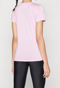 Lichtroze sportt-shirt met korte mouwen, ronde halslijn en een klein logo op de achterkant; gecombineerd met zwarte leggings.