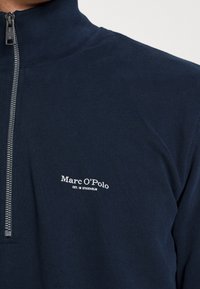 Pullover zip-up blu navy realizzato in tessuto a coste, con colletto alto, zip argentata e testo del logo bianco sul petto.