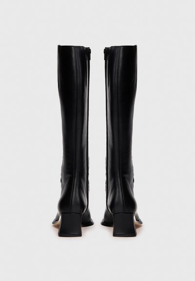 Μαύρες δερμάτινες μπότες μέχρι το γόνατο με τετράγωνο τακούνι, με λεία επιφάνεια, κατακόρυφες ραφές και φερμουάρ στο πίσω μέρος.
