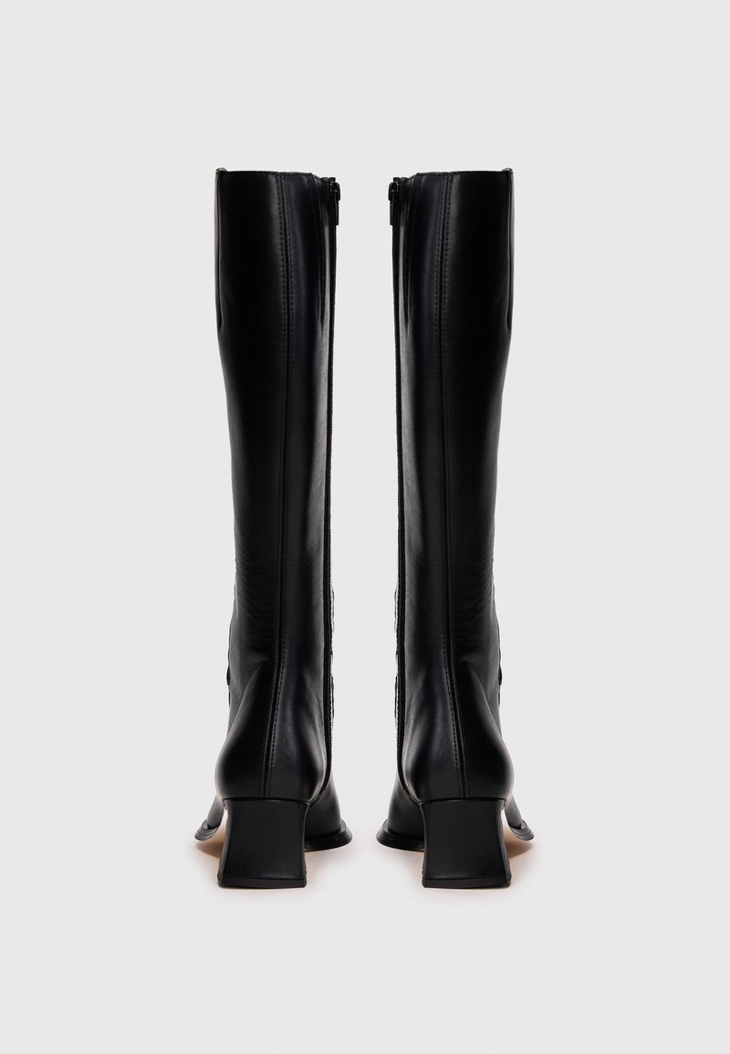 Schwarze kniehohe Stiefel aus Leder mit quadratischem Absatz, die eine glatte Oberfläche, vertikale Nähte und einen Reißverschluss auf der Rückseite aufweisen.