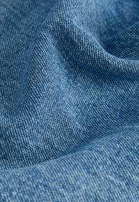 Denim tkanina u nijansama plave boje s teksturiranom površinom. Tkanje pokazuje klasični uzorak, naglašavajući mekoću i debljinu tkanine.