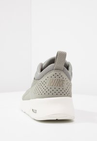 Scarpa sportiva grigia con dettagli in rete e perforazioni. Presenta un colletto imbottito, una suola bianca a contrasto e un discreto logo "NIKE" sul tallone.