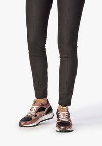 Sportovní tenisky kombinující kovově růžovou zlatou a černé materiály, s bílými tkaničkami a silnou černou podrážkou.