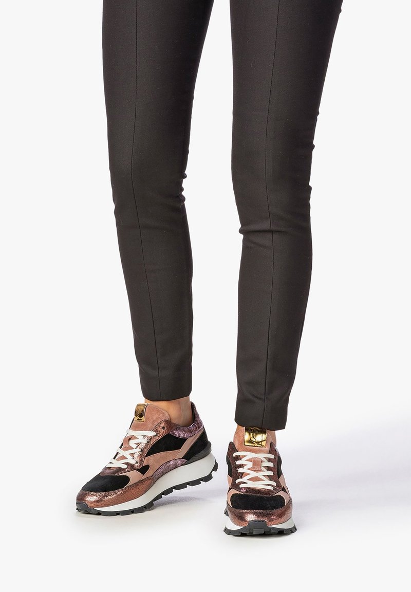 Sportovní tenisky kombinující kovově růžovou zlatou a černé materiály, s bílými tkaničkami a silnou černou podrážkou.