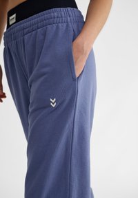 Lichtblauwe sweatpants met een elastische zwarte tailleband, zijzakken en een kleine witte chevronlogo op de dij. Gladde textuur, casual pasvorm.