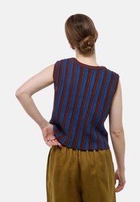 Haut en tricot sans manches rayé marron et bleu avec un col rond, présentant un tissu texturé et une coupe décontractée, associé à un pantalon beige clair.