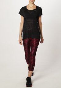 Camiseta atlética negra de corte holgado, combinada con leggings de patrón rojo y negro. El calzado son zapatillas negras.