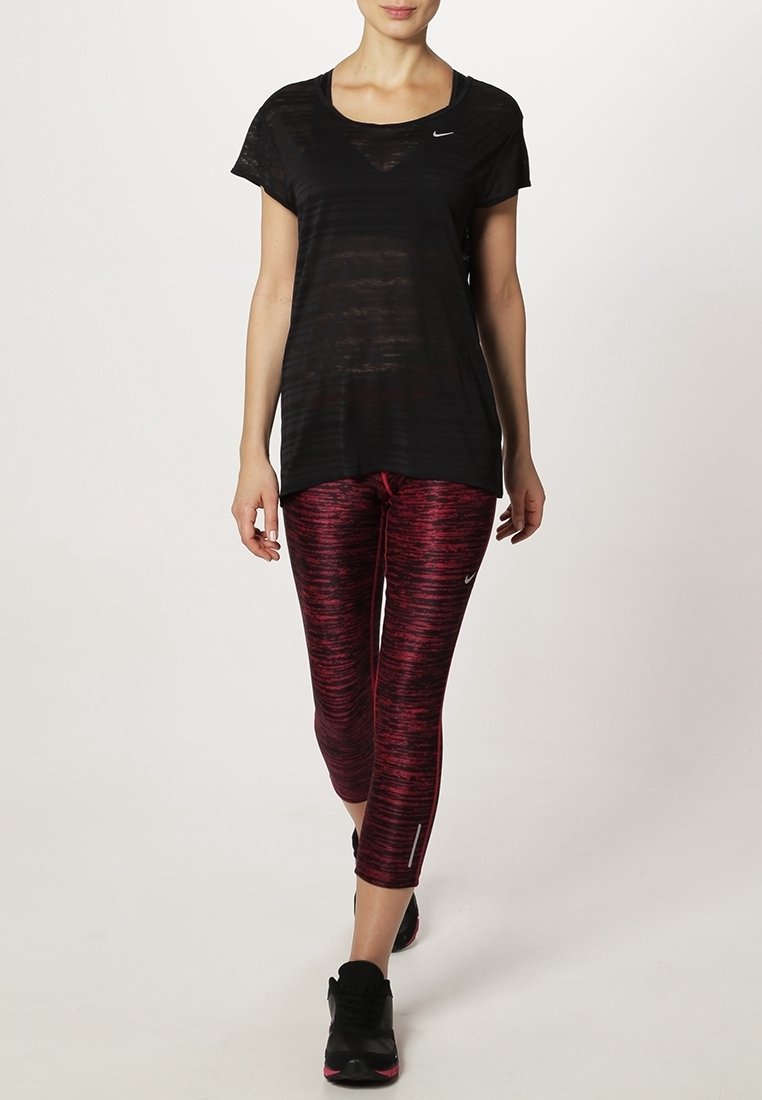 Camiseta atlética negra de corte holgado, combinada con leggings de patrón rojo y negro. El calzado son zapatillas negras.