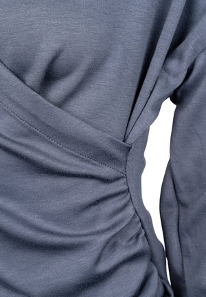 Szary longsleeve z marszczeniem po boku, wykonany z miękkiego, teksturowanego materiału. Detale szwów podkreślają sylwetkę.
