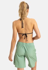 Bikini top s čiernymi šnúrkami a zelenými plážovými šortkami. Šortky majú elastický pás a bočné rozparky pre pohodlný pohyb.