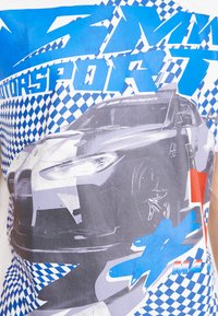 White T-shirt featuring a graphic of a car in shades of gray, with blue text and checkerboard pattern details in blue and white.