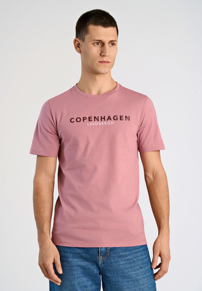 Rosa bomull T-shirt med "KÖPENHAMN" i mörka bokstäver, rundad halsringning och korta ärmar, tillsammans med blå jeans.