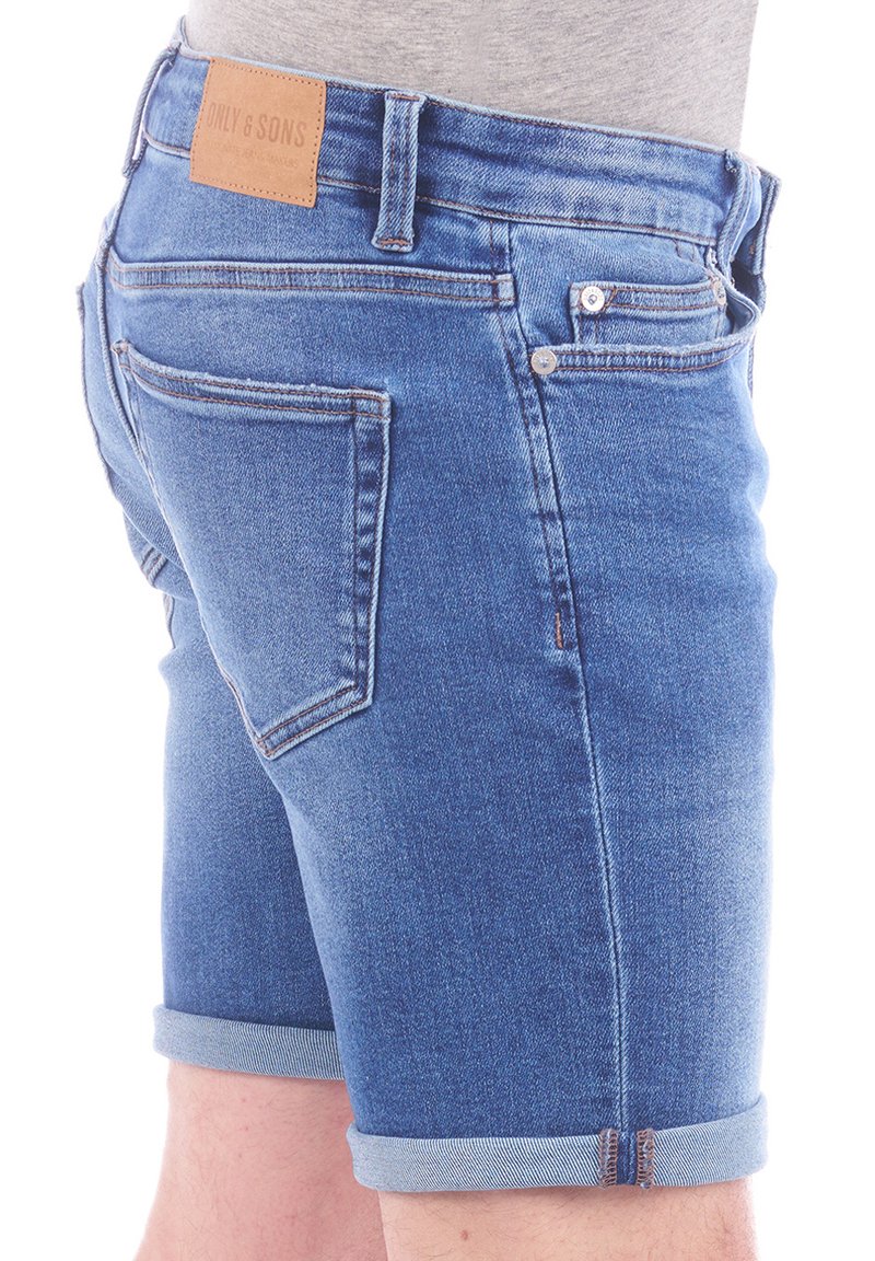 Shorts en denim bleu moyen avec un ourlet roulé, dotés d'une étiquette en cuir à la taille et d'un design classique à cinq poches.