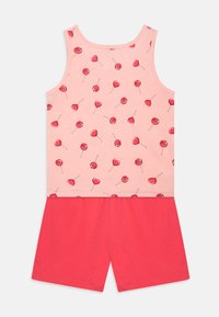 Canotta di cotone rosa chiaro con motivo di cuori e lecca-lecca, abbinata a pantaloni corti rossi brillanti. Entrambi hanno una consistenza morbida e una vestibilità casual.