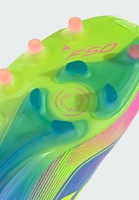 Football boot sole, featuring a bright green base with pink accents. Textured, transparent elements and multiple studs for traction.