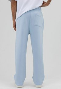 Pantalon de survêtement bleu clair à coupe décontractée, taille élastique et une poche arrière unique. Fabriqué en matériau doux avec une texture lisse.