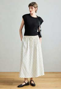 Μαύρο πλεκτό τοπ με κοντά μανίκια σε συνδυασμό με λευκή μακριά φούστα που έχει πουά σχέδιο, ελαστική μέση και τσέπες. Μαύρα επίπεδα παπούτσια.