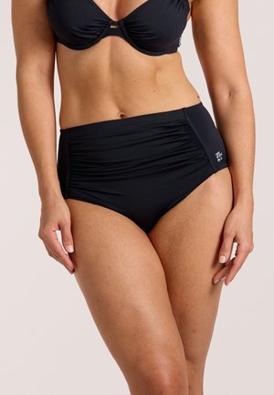 Žena u crnim visokim bikini gaćicama s naborima i odgovarajućem gornjem dijelu bikinija, stoji s opuštenim rukama uz tijelo.