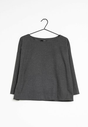 T-shirt gris à manches longues présenté sur un cintre noir. Il possède un large col, une coupe décontractée et une texture douce et lisse.