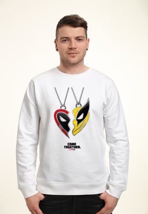 Man wearing white sweatshirt with graphic of red and yellow half-heart necklace pendants labeled Best Friends and text "Come Together Marvel Studios."