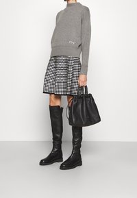Szary sweter z wysokim dekoltem, spódnica w czarno-białą kratę houndstooth, czarne skórzane botki do kolan i czarna torba na sznurku.