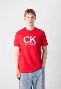 Raudona medvilninė marškinė su balta "CK CALVIN KLEIN" Logo priekyje, trumpomis rankovėmis ir klasikinės apvalios iškirptės.