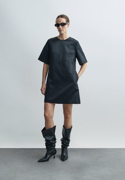 Robe courte en cuir noir avec un col rond et des manches courtes, associée à des bottes noires décontractées montant jusqu'aux genoux. Texture lisse et design minimaliste.