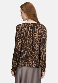Leopardenmuster Bluse aus braunem und schwarzem Seidenstoff, mit rundem Ausschnitt, langen Ärmeln, gerafften Bündchen und lockerer Passform mit Falten an der Rückseite.