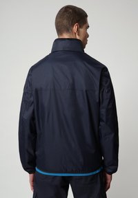Giacca impermeabile blu navy con colletto alto, polsini elasticizzati e un'accentuazione a contrasto in teal in vita. Texture liscia e design semplice.