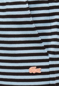 Tissu tricoté à rayures horizontales bleues et noires avec un petit logo de crocodile rose brodé près d'une couture.