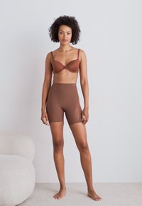 Καφέ σετ εσωρούχων που περιλαμβάνει σουτιέν με ρυθμιζόμενες τιράντες και ταιριαστά ψηλόμεσα σορτς, αμφότερα με λεία ματ επιφάνεια.