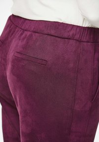 Paarse suède broek met een elastische tailleband, met een enkele paspelzak aan de achterkant, met een soepele, zachte textuur.