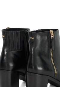 Black leather ankle boots with a high heel, featuring side zippers, vertical ribbed texture, and gold hardware accents.