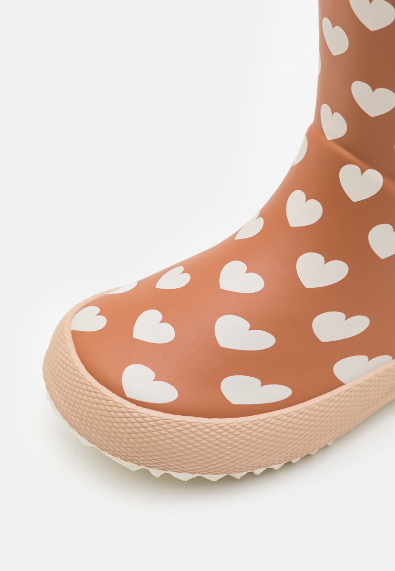 Oranje rubberen laars met een wit hartpatroon, ronde neus, gestructureerde buitenzool voor grip en een contrasterende lichtroze zoolrand.