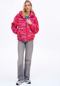 Puszysta, różowa i fioletowa bluza z kapturem na zamek, noszona na niebieskiej koszulce, w połączeniu z szarymi spodniami i adidasami.