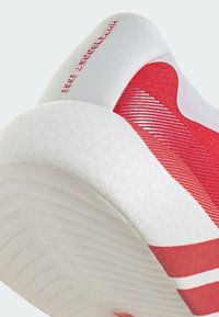 Gros plan sur le talon d'une basket blanche et rouge avec une semelle texturée et le texte "HYPERBOOST ZONE" sur le col rembourré du talon.