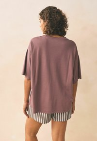 Labava majica kratkih rukava od mješavine pamuka u boji mauve, uparena s kratkim hlačama u sivoj i bijeloj prugastoj kombinaciji. Mekana tekstura s opuštenim siluetom.